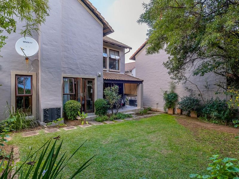 A private rear garden featuring a lawn, established trees, and a covered patio area attached to the main house structure.