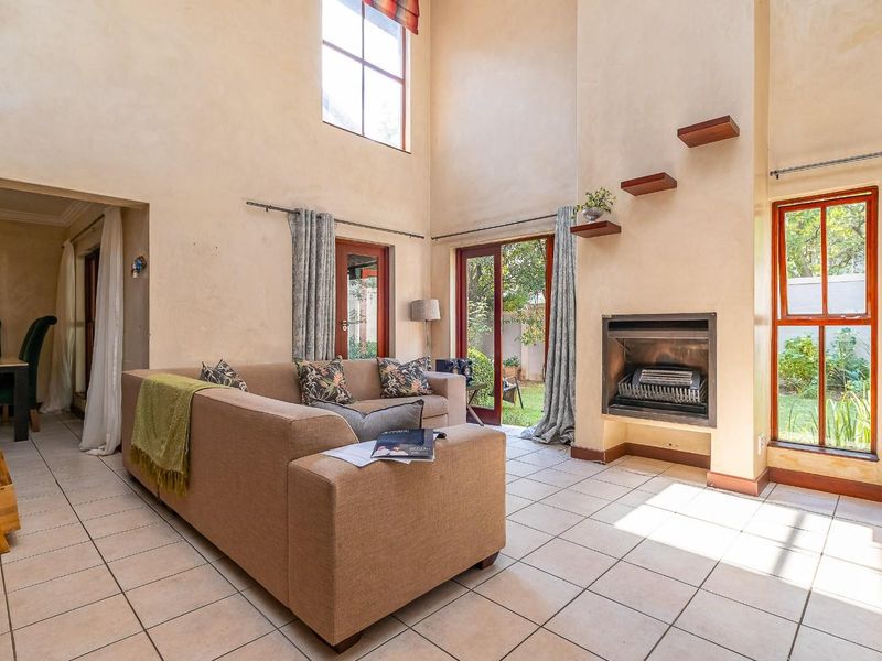 Spacious double-volume living room featuring a built-in fireplace, tiled flooring, and large windows providing direct access to the rear garden.
