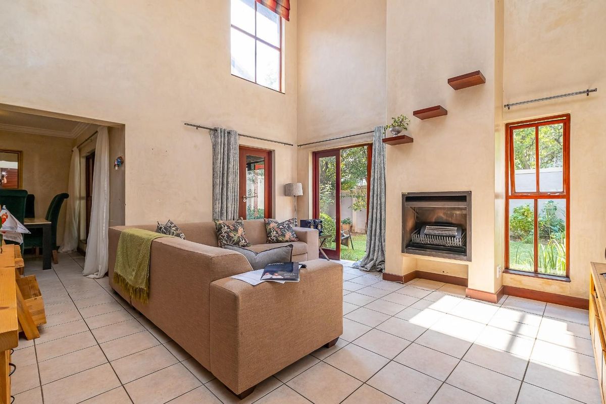 Spacious double-volume living room featuring a built-in fireplace, tiled flooring, and large windows providing direct access to the rear garden.