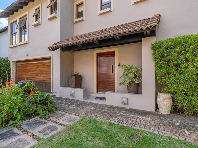 Front entrance of the house featuring a wooden door, tiled roof overhang, paved walkway, and integrated garage door.