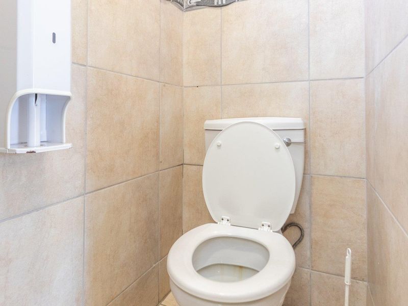 A compact commercial restroom featuring floor-to-ceiling beige ceramic wall tiles and a standard white porcelain toilet.