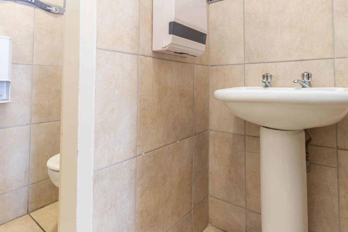 A functional commercial restroom featuring a pedestal basin, tiled walls, and a separate toilet cubicle with wall-mounted soap and paper towel dispensers.