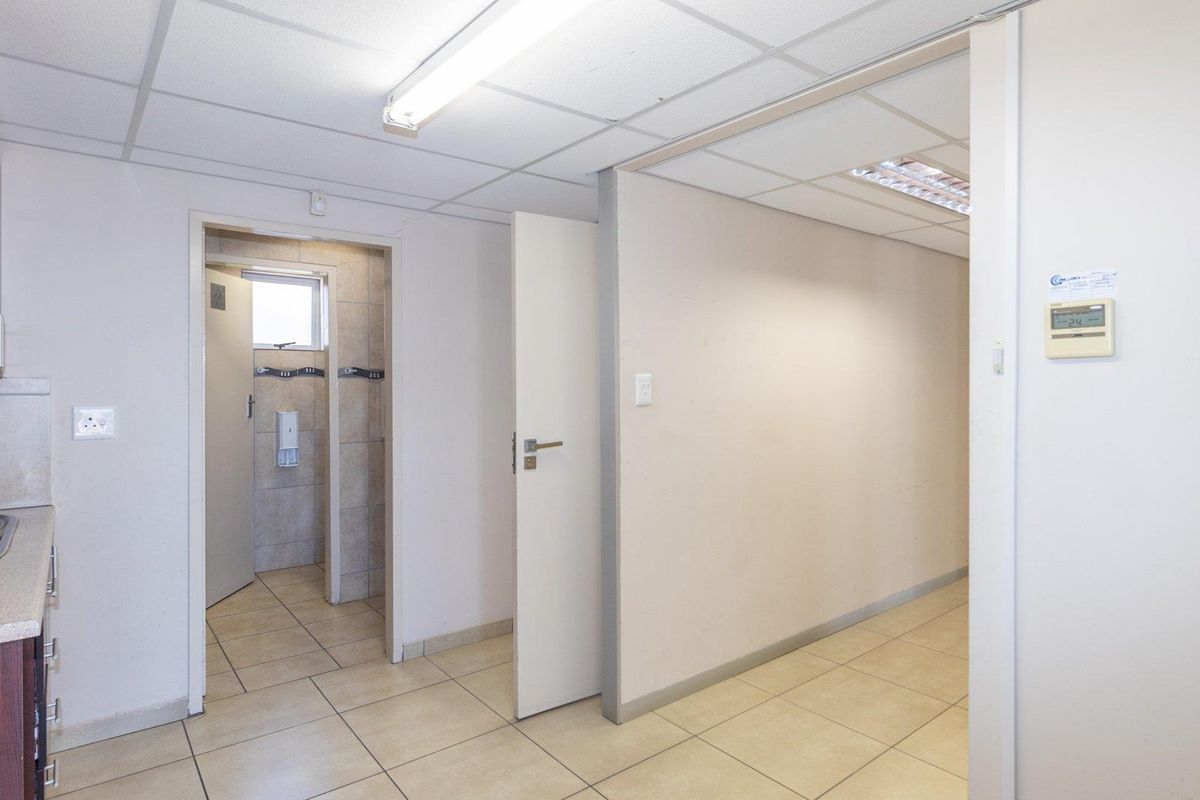 A functional commercial kitchenette area featuring built-in cabinetry, a stainless steel sink, and tiled flooring, leading into a separate utility or restroom space.