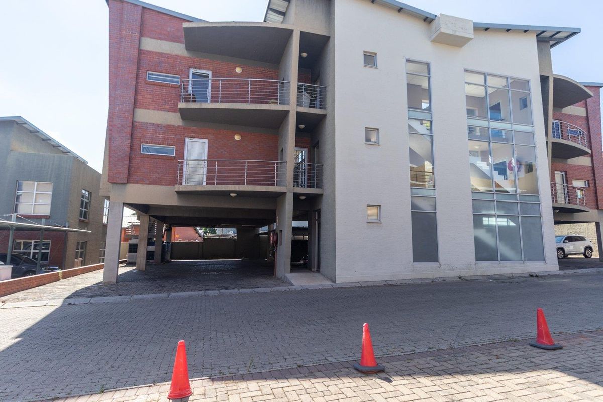 Exterior view of a multi-story commercial building featuring brick and plaster facade, balconies, and ground-level covered parking area.