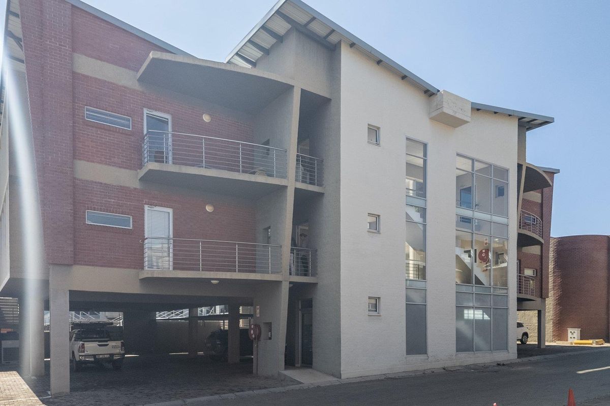 Modern multi-story commercial building featuring a combination of face brick and rendered facade, integrated balconies, and covered ground-level parking.