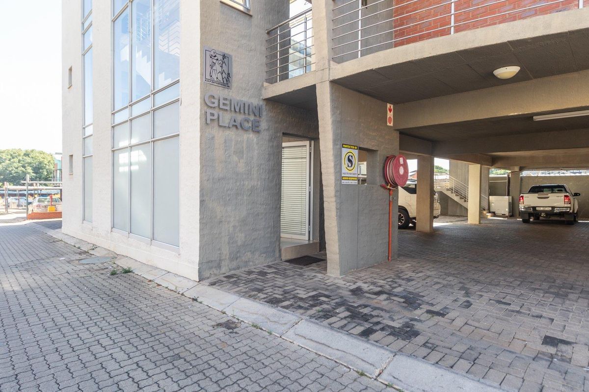 Exterior view of Gemini Place commercial building featuring a paved driveway, covered parking area, and modern glass facade.