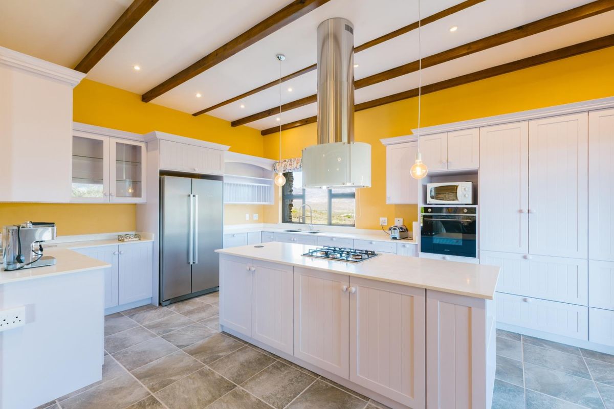 Modern kitchen featuring a central island with a built-in gas hob, stainless steel extractor fan, white cabinetry, and exposed wooden ceiling beams.