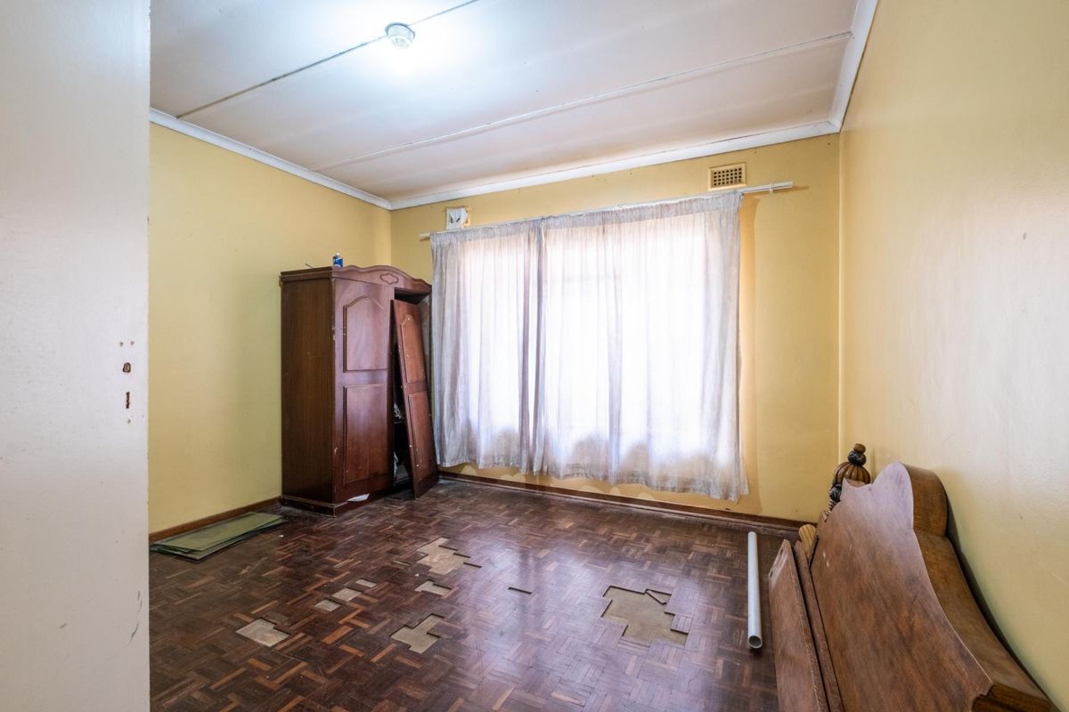 A bedroom featuring parquet flooring with visible damage and missing sections, requiring restoration or replacement to improve the space.