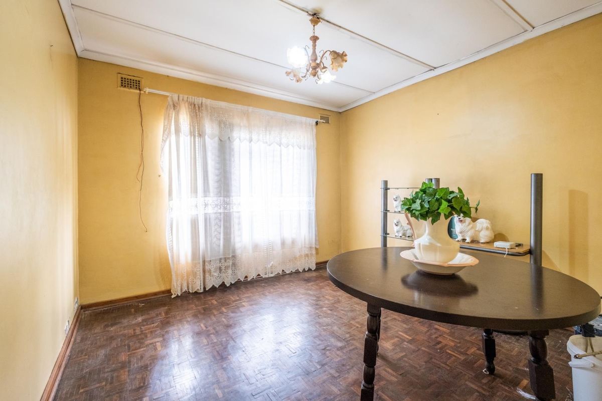A dated living room featuring original parquet flooring, yellow wall finishes, and a traditional ceiling design, offering a blank canvas for renovation.