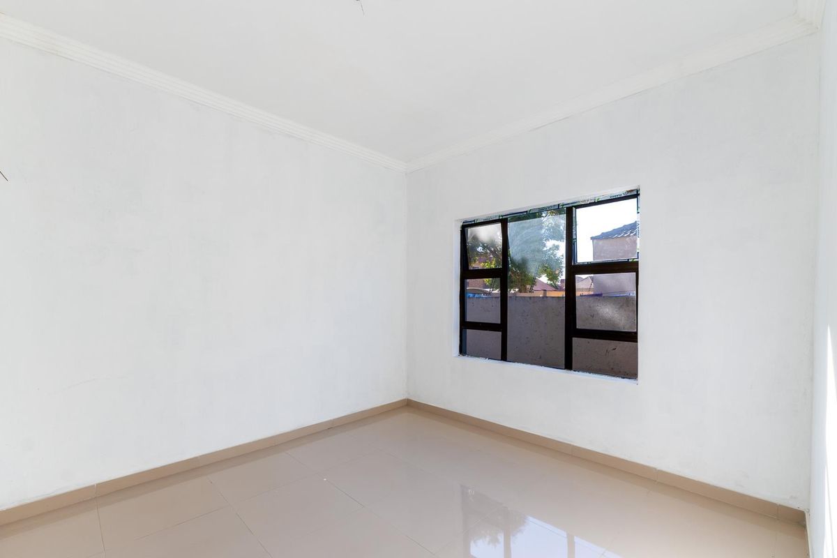 A bright, empty bedroom featuring neutral tiled flooring, white walls, and a dark-framed window.