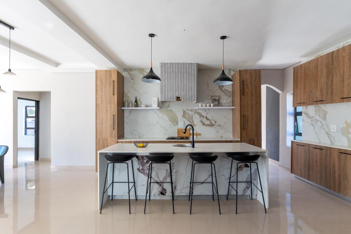 Modern open-plan kitchen featuring wood-grain cabinetry, marble-look splashbacks, a central island with a sink, and integrated lighting.