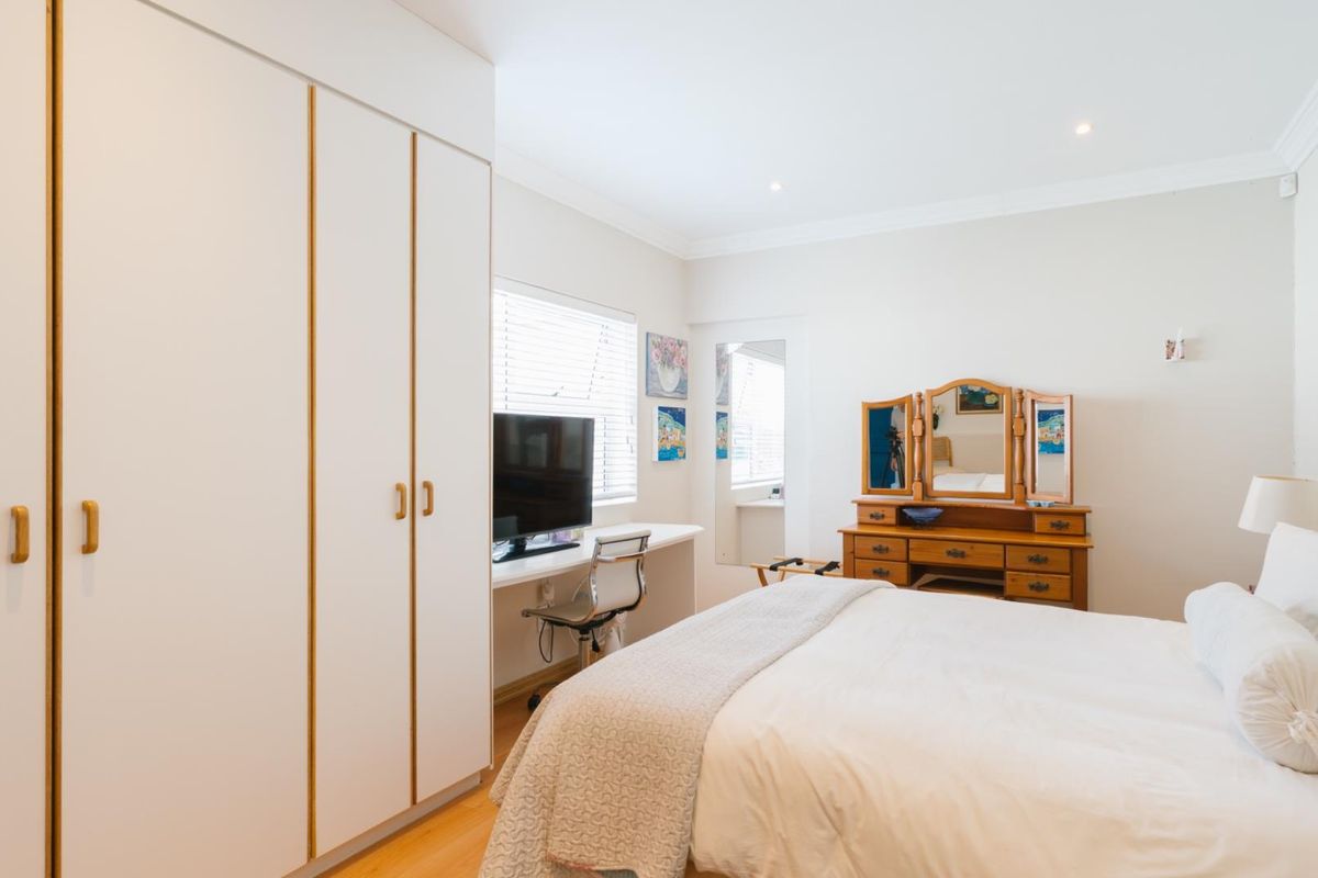A bright bedroom featuring built-in floor-to-ceiling wardrobes, laminate flooring, and a built-in desk area under the window.