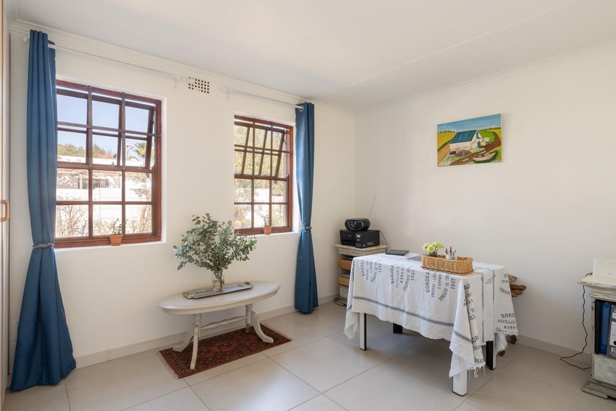 A bright bedroom featuring tiled flooring, built-in cupboards, and timber-framed windows that provide natural light.