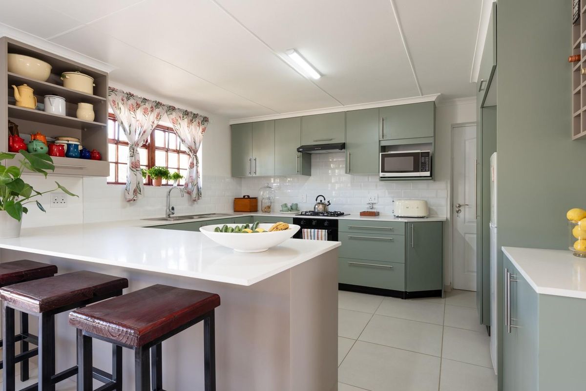 Modern kitchen featuring sage green cabinetry, white stone countertops, subway tile backsplash, built-in oven, and a breakfast bar island.