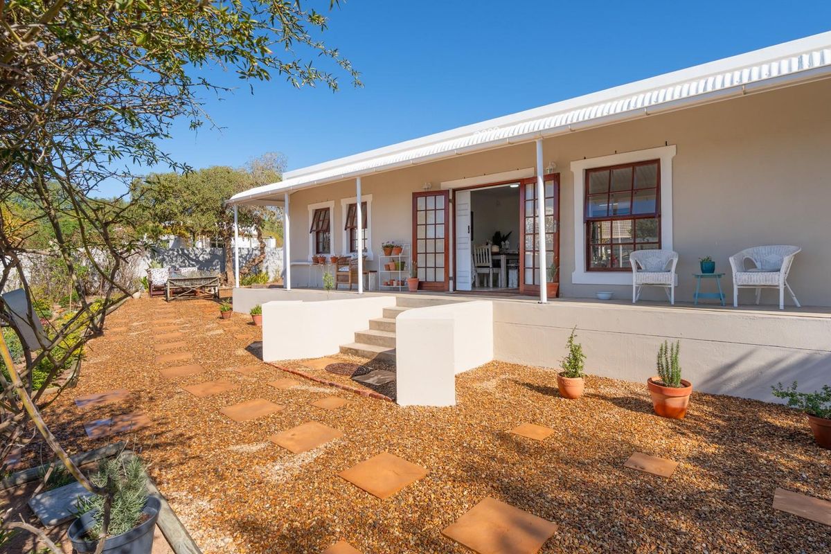 A well-maintained rear exterior view featuring a covered patio with steps leading down to a landscaped garden area with gravel and stone pavers.