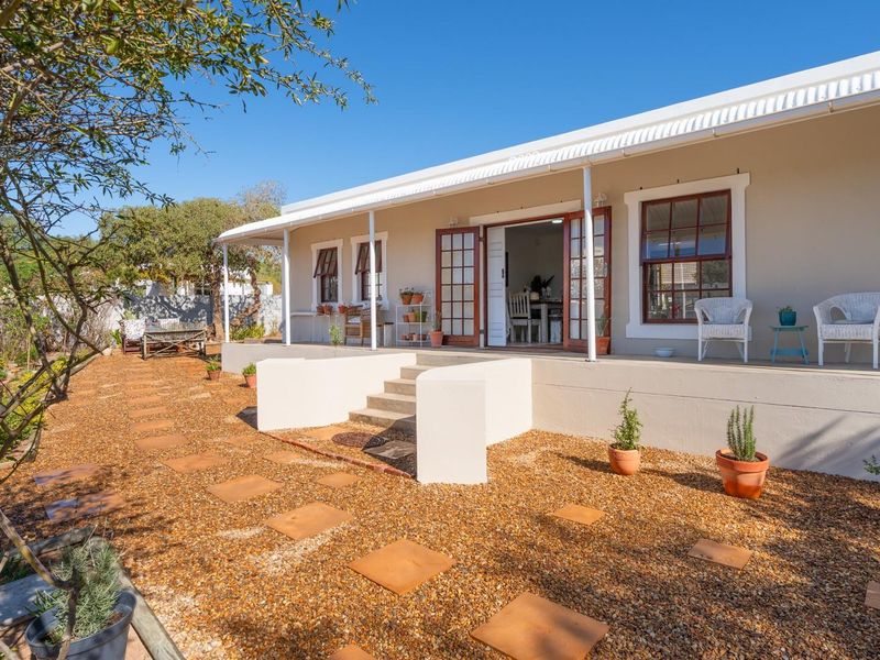 A well-maintained rear exterior view featuring a covered patio with steps leading down to a landscaped garden area with gravel and stone pavers.