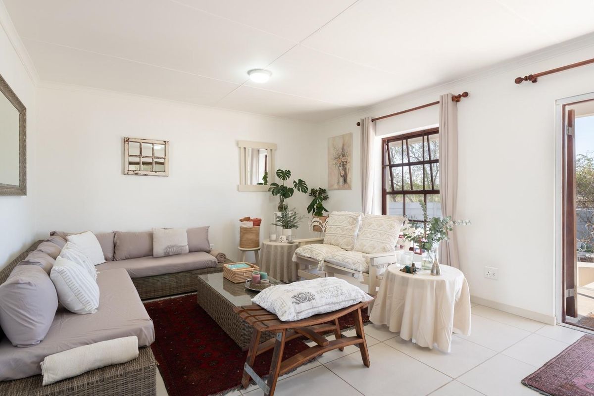 A bright living room featuring tiled flooring, large windows, and a glass door providing direct access to the outdoor patio area.
