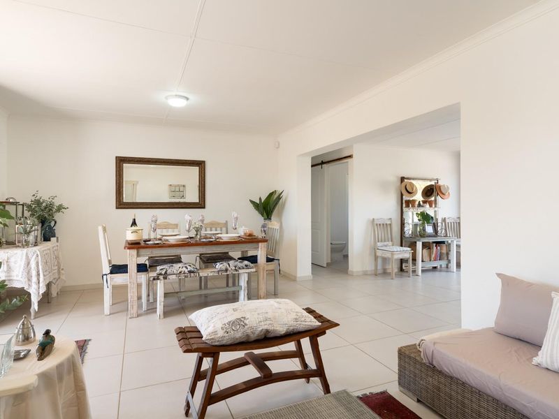 An open-plan living and dining area featuring neutral ceramic floor tiles, recessed transition between spaces, and access to an adjacent bathroom.