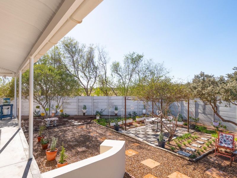 A covered patio overlooking a landscaped rear garden featuring gravel pathways, established trees, and a paved seating area enclosed by a perimeter wall.