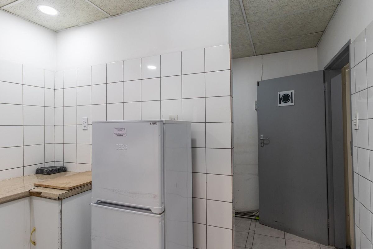 A functional commercial kitchenette area featuring tiled walls, a stone-look countertop, and a drop ceiling, providing basic utility space for staff or office use.