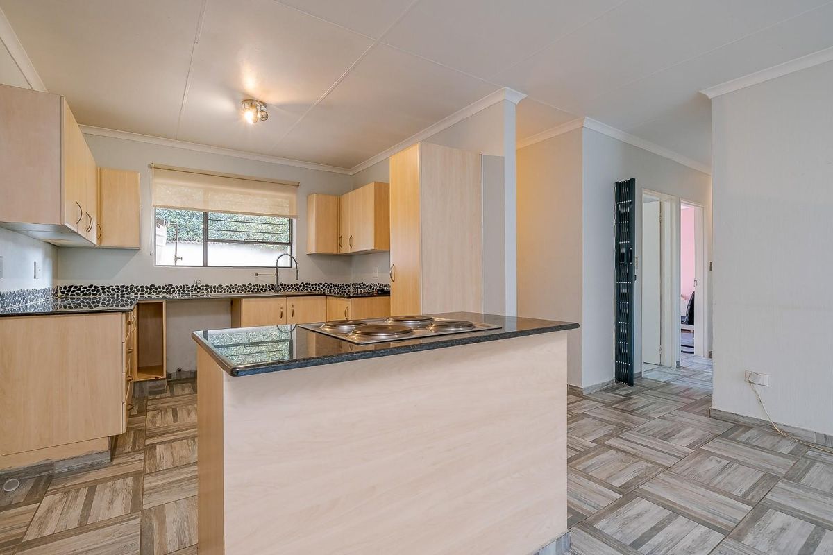 Functional kitchen featuring light wood cabinetry, granite countertops, a central island with a built-in hob, and tiled flooring throughout.
