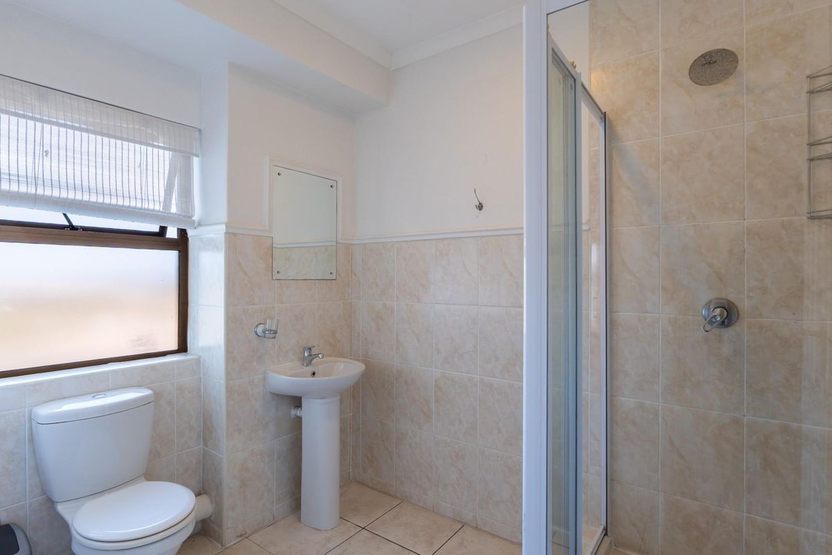 A functional bathroom featuring a pedestal basin, a glass-enclosed shower, and a toilet, finished with neutral wall and floor tiling.