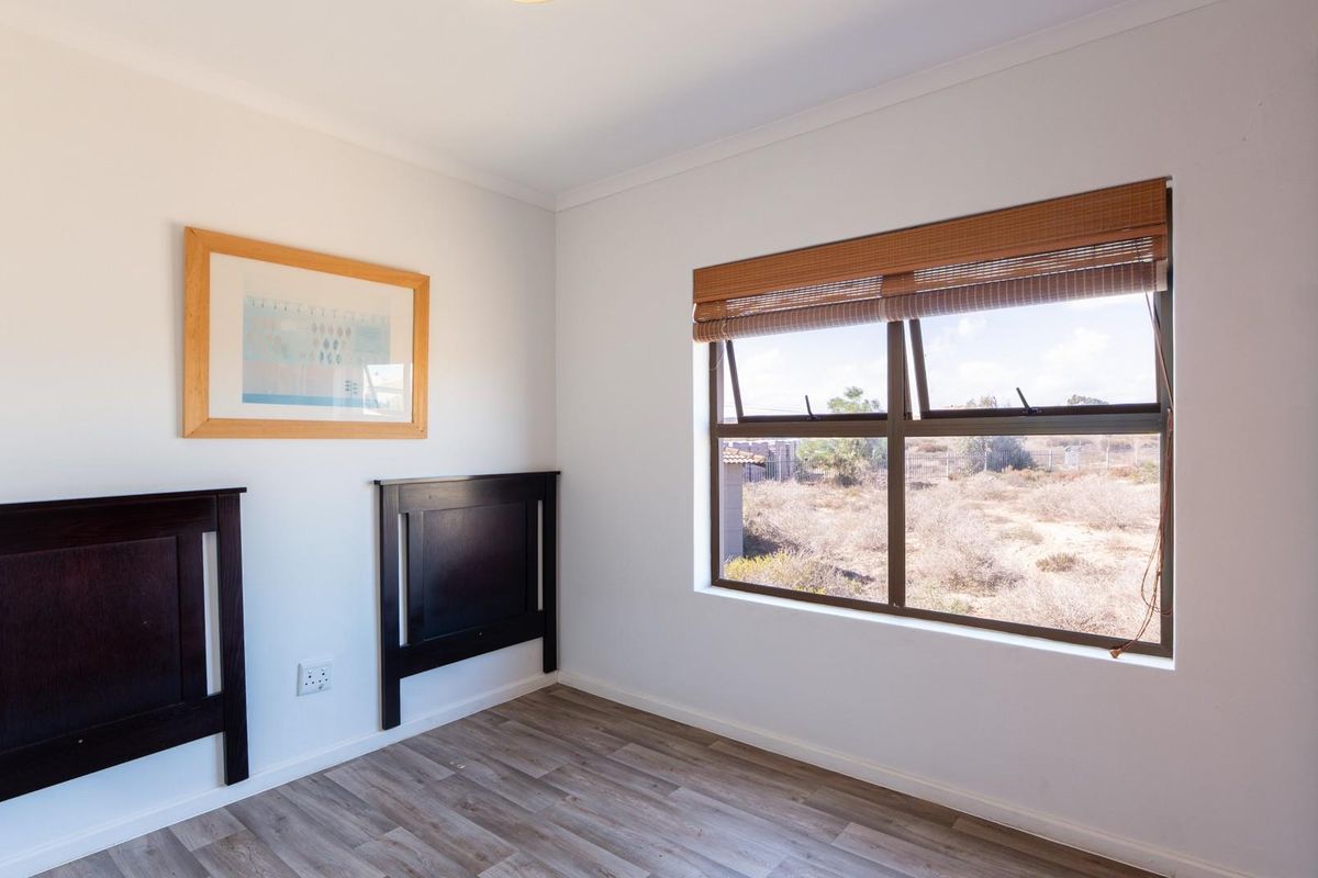 A bright bedroom featuring wood-look laminate flooring, a large window with a roller blind, and built-in cabinetry.