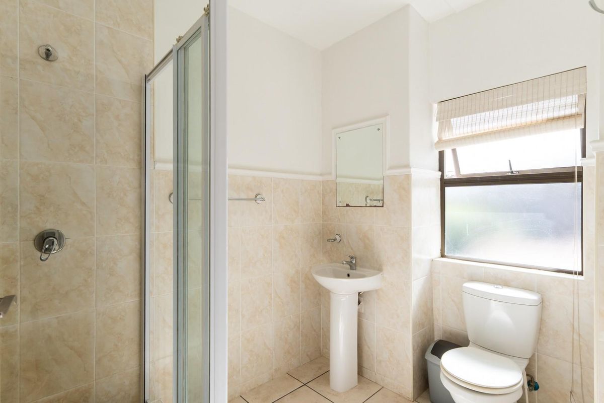 A functional bathroom featuring a glass-enclosed shower, pedestal basin, and toilet, finished with neutral wall and floor tiling.