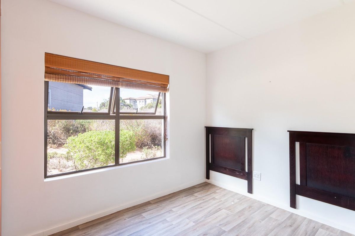 A bright bedroom featuring wood-look laminate flooring, a built-in cupboard, and a window with a bamboo blind.