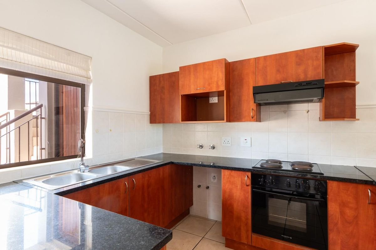 A functional kitchen featuring dark granite countertops, wooden cabinetry, a built-in oven with hob, and an extractor fan.