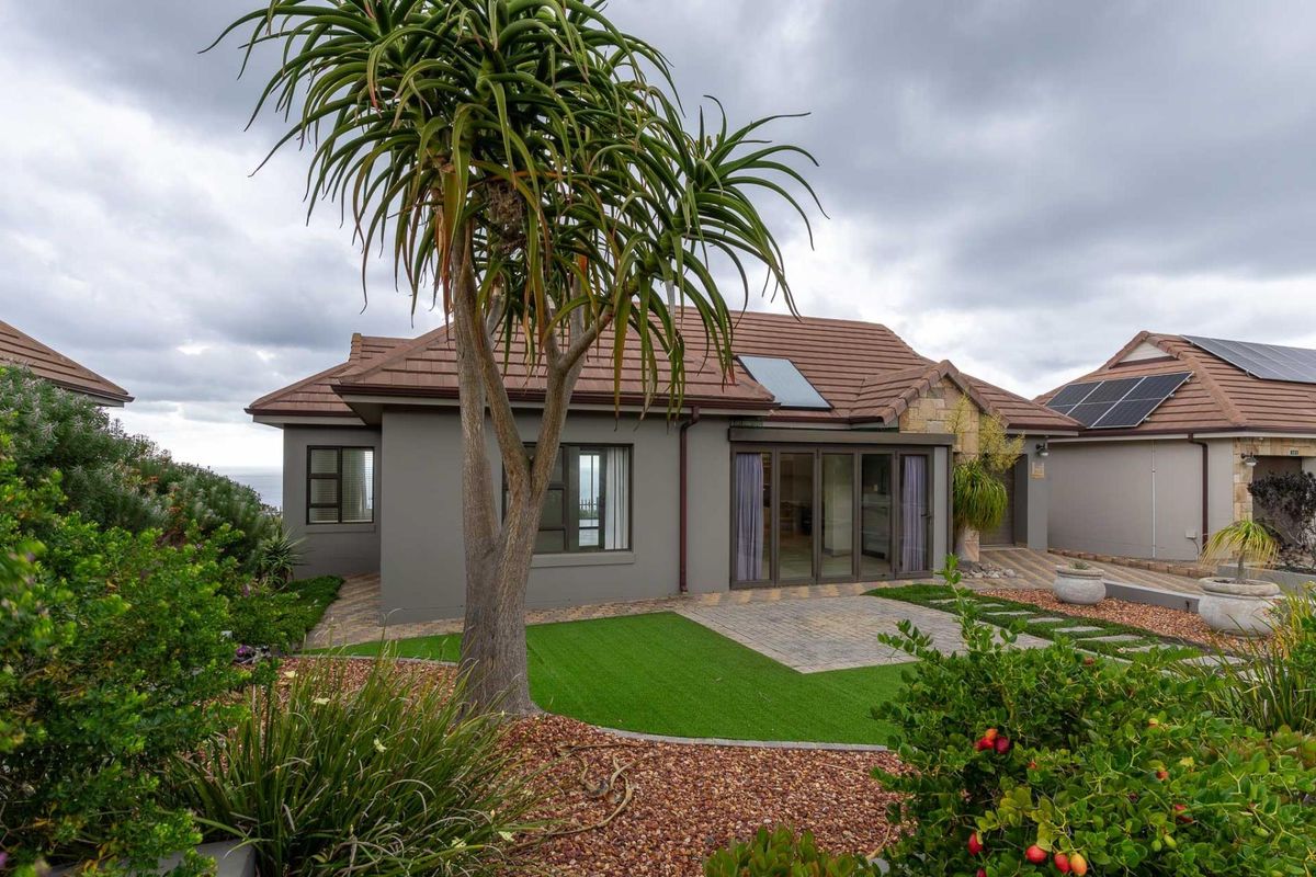 Rear view of a modern single-story house featuring a paved patio, artificial lawn, and solar panels on the tiled roof.