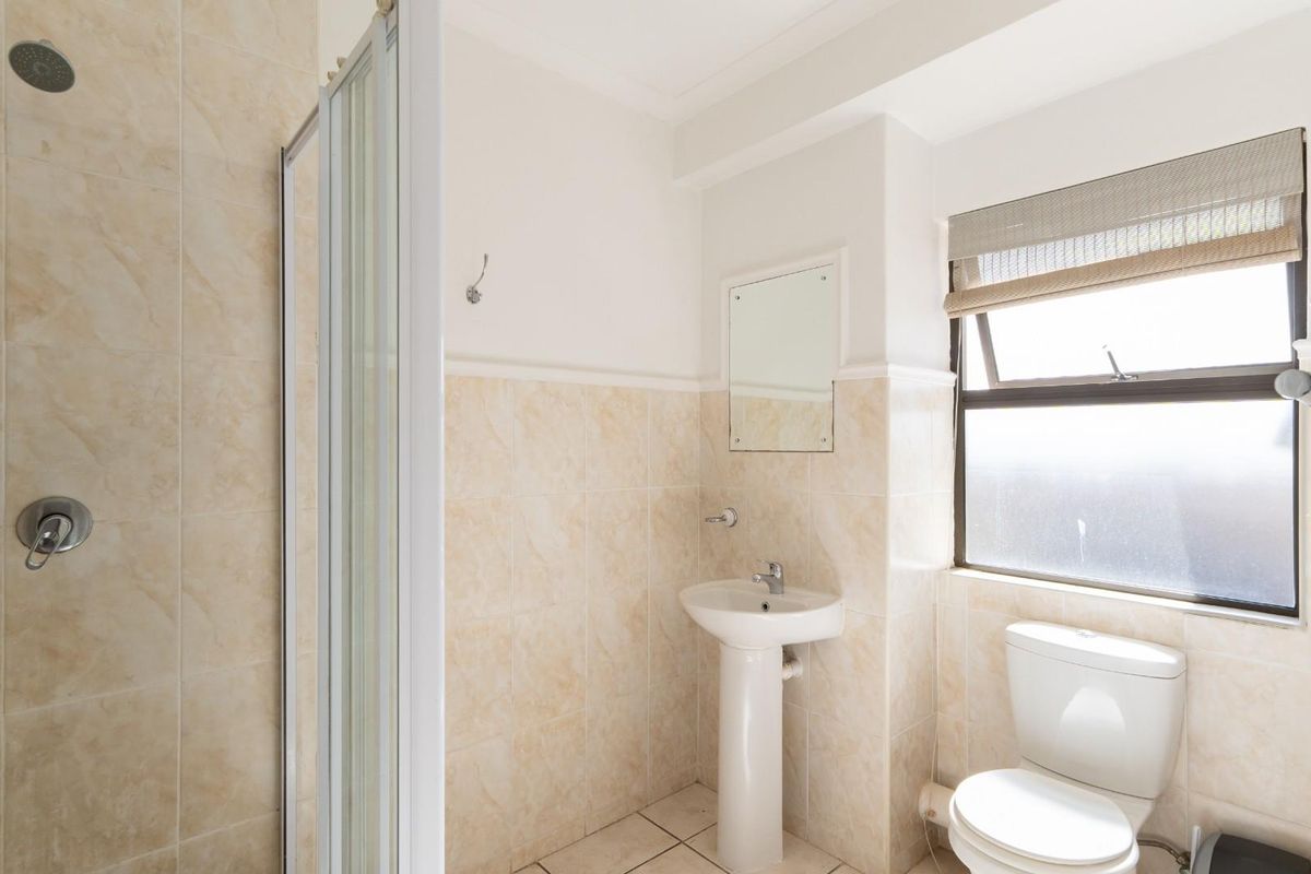 A functional bathroom featuring a pedestal basin, a toilet, and a tiled shower enclosure with a glass door.