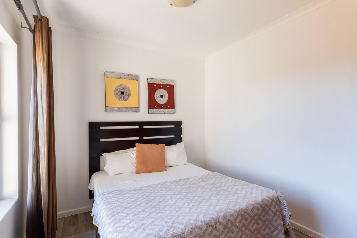 A functional bedroom featuring neutral walls, wood-look flooring, and a window with curtain tracks.