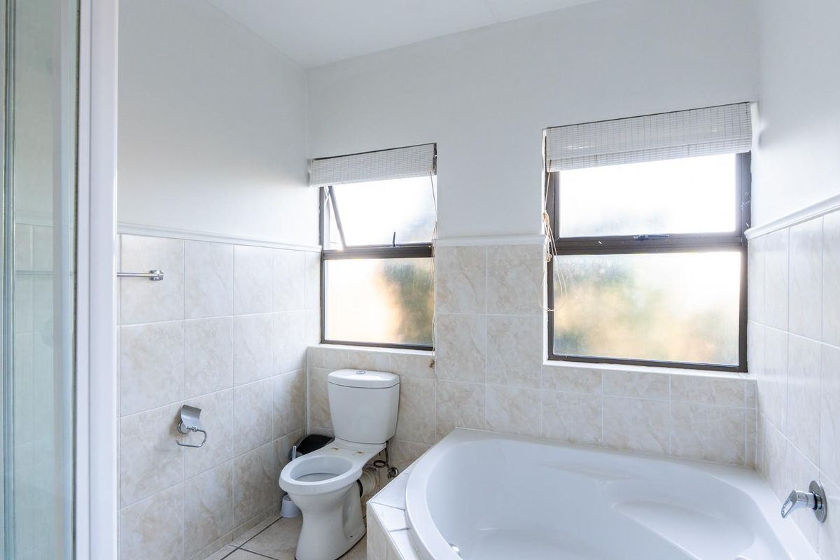 A functional bathroom featuring a corner bathtub, a separate shower enclosure, and a standard toilet with tiled walls and natural light.