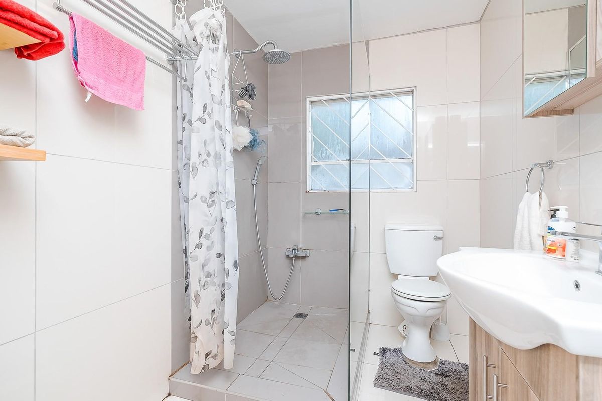 A functional bathroom featuring a walk-in shower with glass partition, wall-mounted shower head, vanity basin, and toilet with security bars on the window.