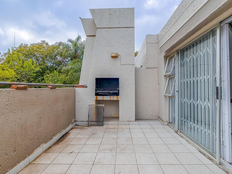 A covered balcony featuring a built-in braai, tiled flooring, and sliding door access to the interior living space.