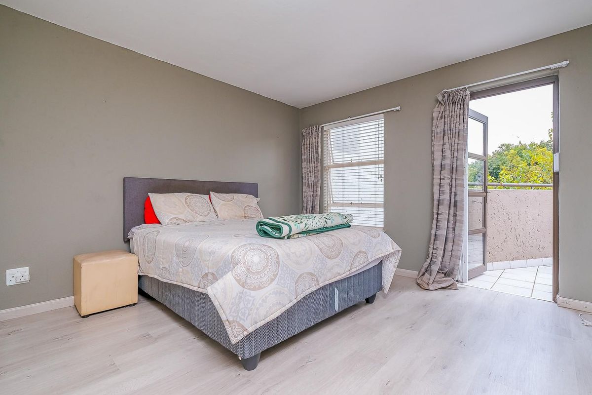 A bedroom featuring light-toned laminate flooring, neutral wall paint, and direct access to a private balcony through a glass door.