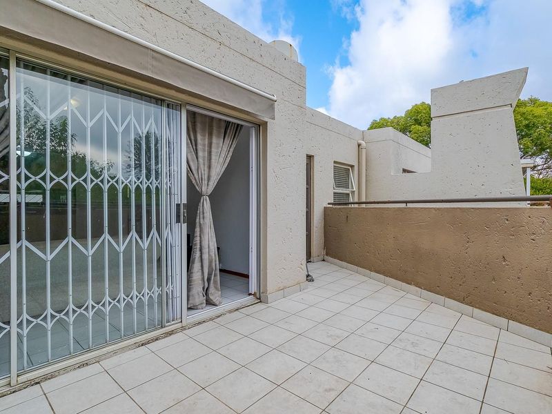 A private balcony featuring tiled flooring, a metal security gate, and a solid boundary wall, providing an outdoor extension to the living space.