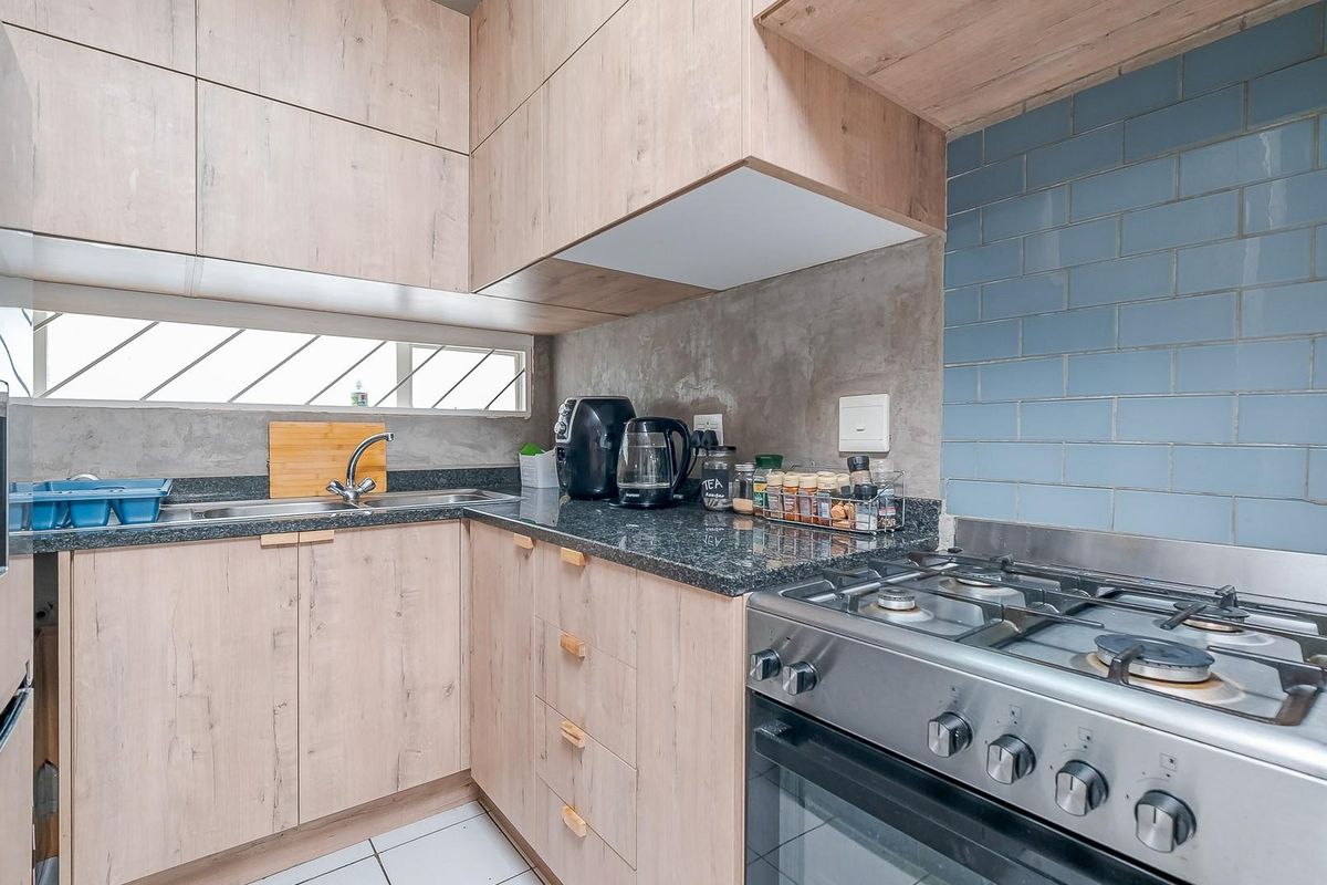 Modern kitchen featuring light wood-grain cabinetry, granite countertops, a gas stove with oven, and a blue subway tile backsplash.