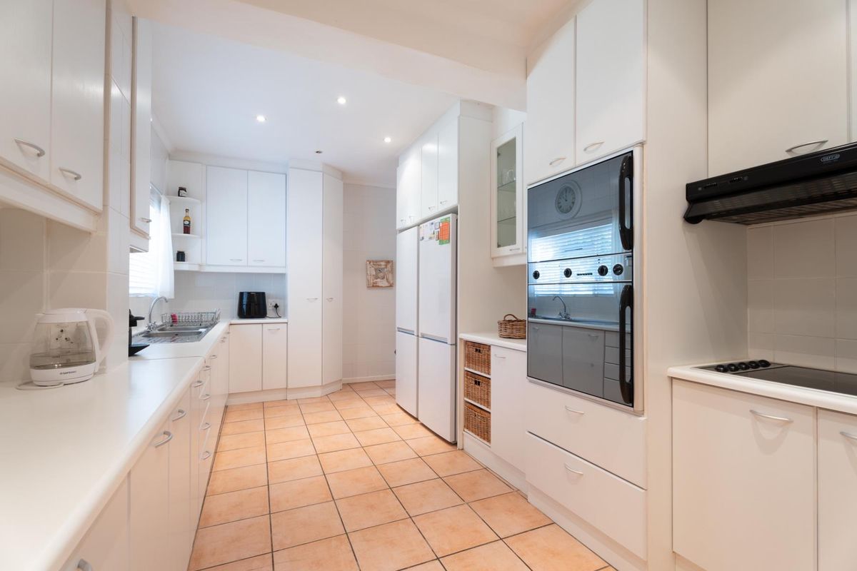 A bright, functional kitchen featuring white cabinetry, built-in oven, integrated hob, extractor fan, and tiled flooring with ample counter space.