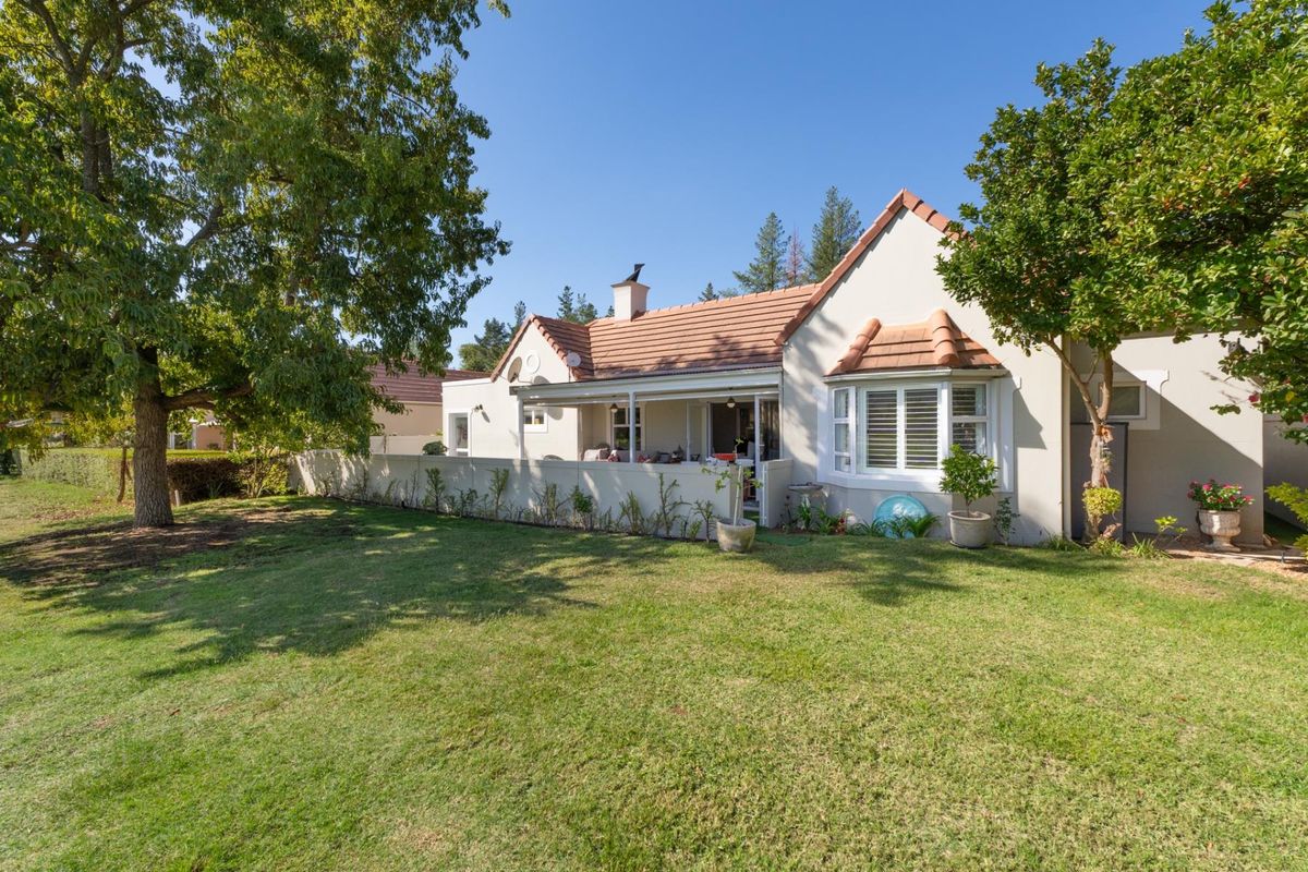 A view of the rear elevation of the house, featuring a covered patio, tiled roof, bay window, and a well-maintained garden.