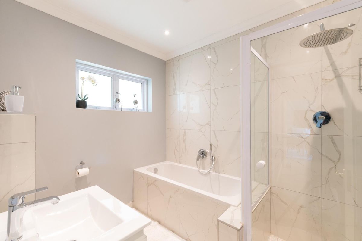 Modern bathroom featuring a tiled bathtub, a separate glass-enclosed shower with a rainfall showerhead, and a contemporary vanity basin.