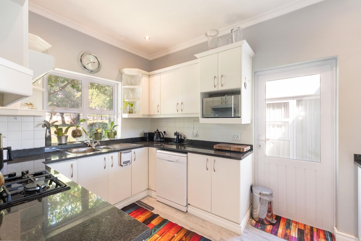 A well-maintained kitchen featuring white cabinetry, dark granite countertops, a built-in gas hob, and direct access to the exterior.