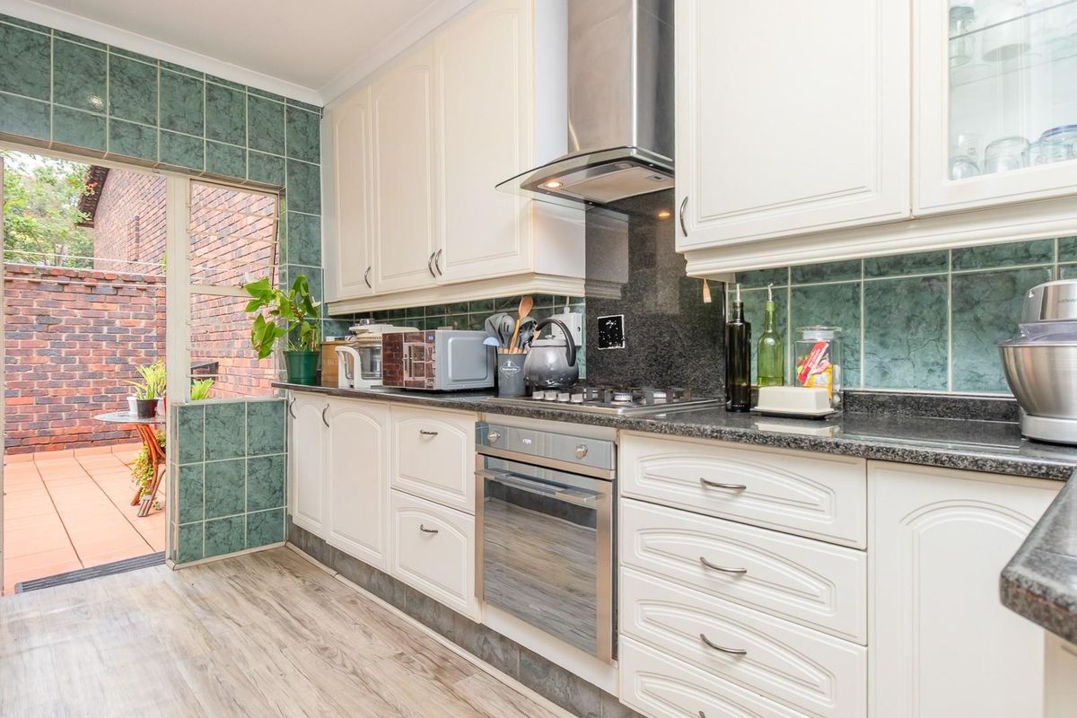 A functional kitchen featuring white cabinetry, granite countertops, a built-in oven, and a stainless steel extractor fan, with direct access to an outdoor patio area.