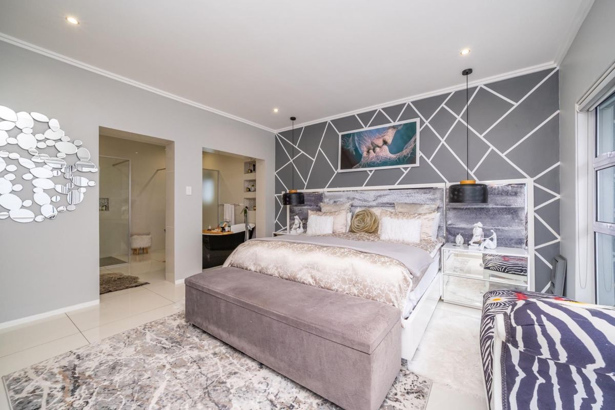 Spacious bedroom featuring a decorative accent wall, recessed downlighting, and an en-suite bathroom with modern tiled finishes.