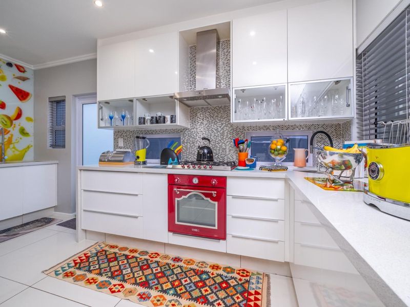 Modern kitchen featuring high-gloss white cabinetry, stone countertops, a mosaic tile backsplash, and a built-in red Smeg oven with stainless steel extractor fan.