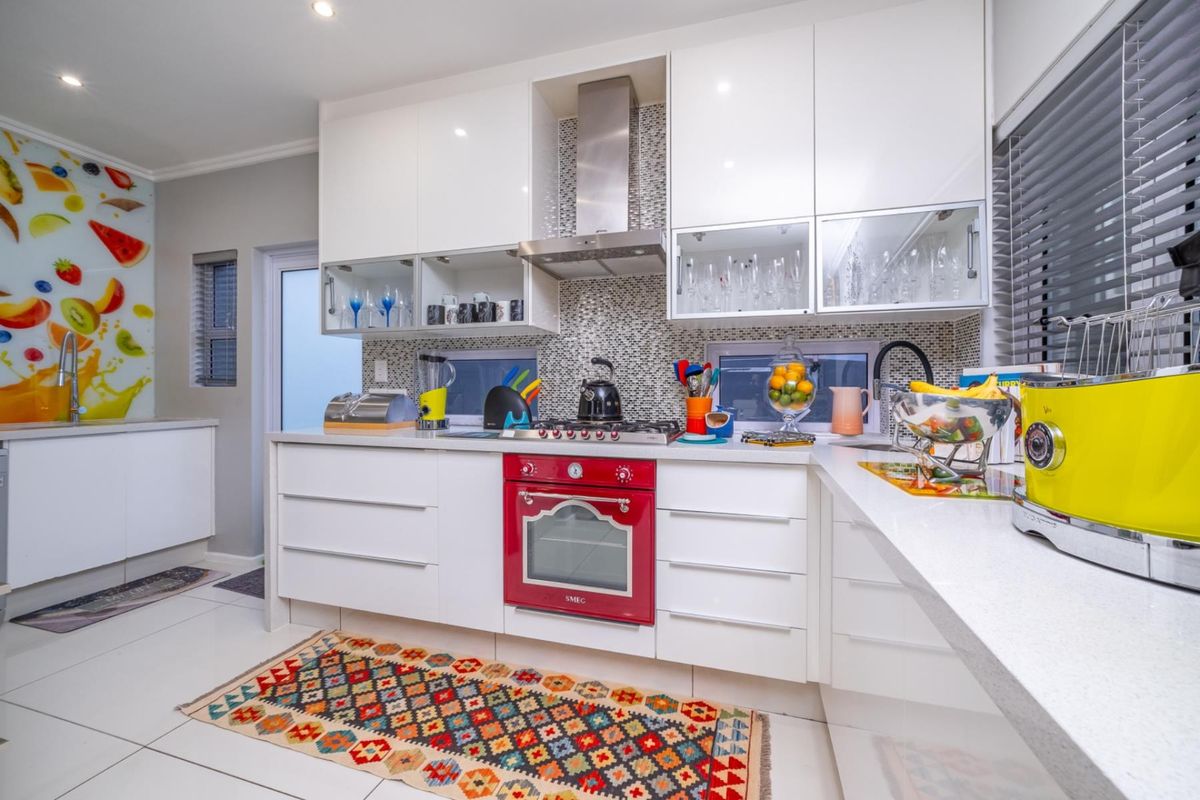 Modern kitchen featuring high-gloss white cabinetry, stone countertops, a mosaic tile backsplash, and a built-in red Smeg oven with stainless steel extractor fan.
