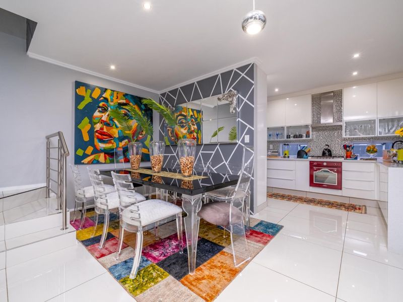 Modern open-plan dining area and kitchen featuring high-gloss cabinetry, stainless steel extractor fan, built-in oven, and polished floor tiles.