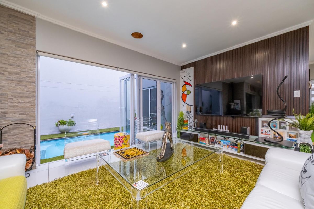 Modern living room featuring large bi-fold doors opening to a private pool area, complemented by a feature stone wall and vertical timber paneling.