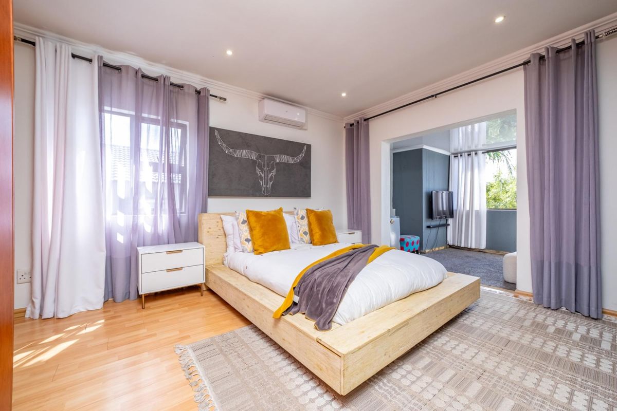 Spacious bedroom featuring light wood flooring, recessed ceiling lighting, and an integrated air conditioning unit, with an adjoining sunroom or study area.